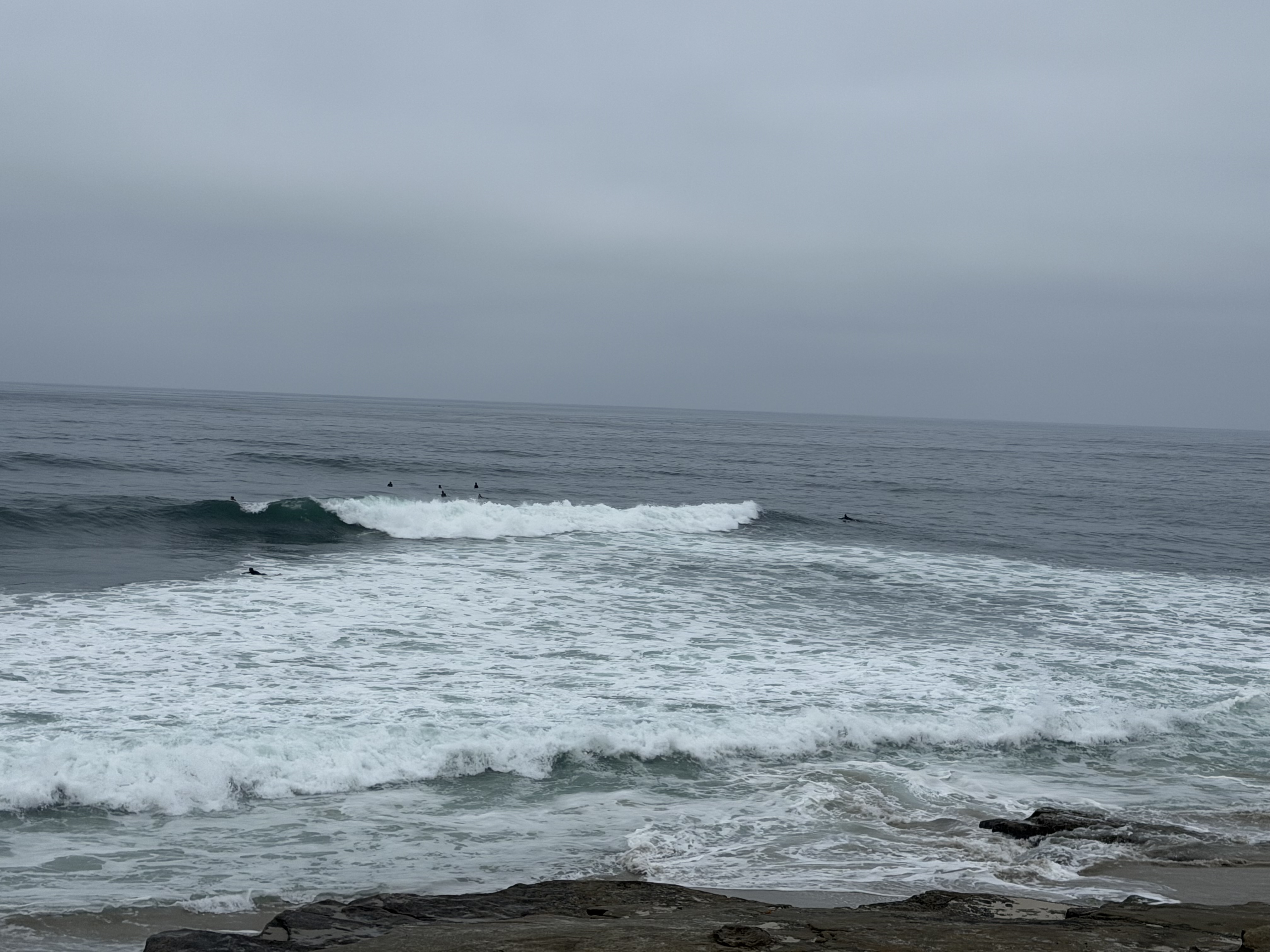Surfers riding waves off the La Jolla coast under a gray sky