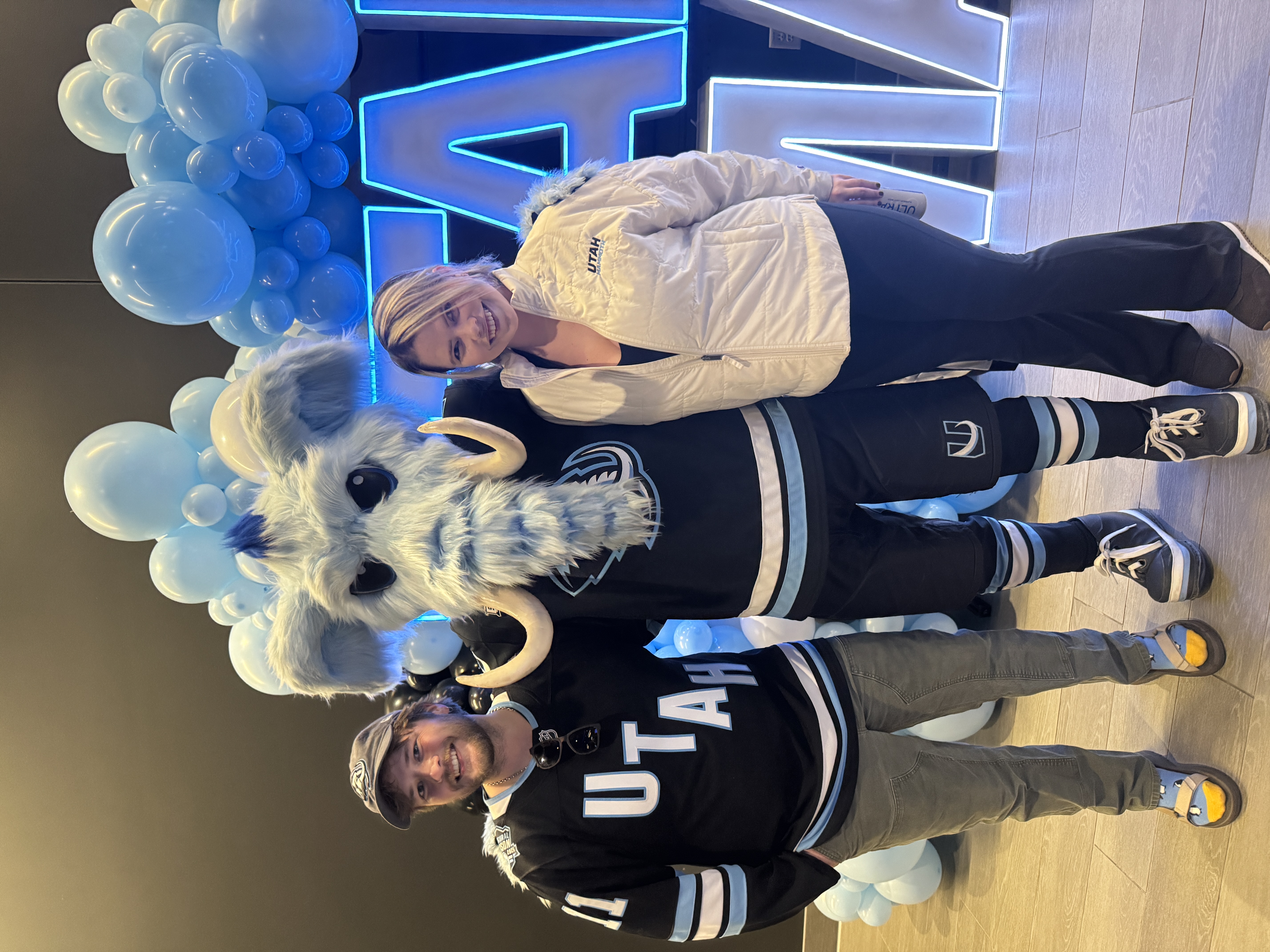 Tusky, the woolly mammoth mascot, posing with two Utah Mammoth fans in front of blue balloons; the featured fan photo.