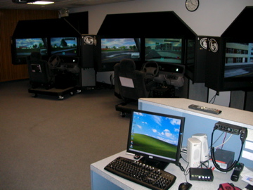 PatrolSim simulator with three road-view displays, a steering wheel, and a driver's seat, shown as the archive's featured installation photograph