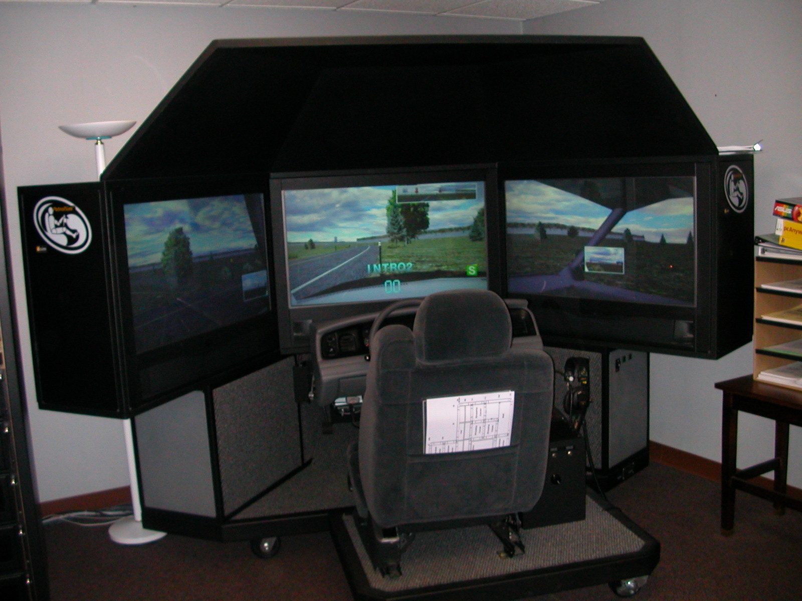 PatrolSim product view showing the enclosed three-screen cockpit, steering wheel, dashboard, and seat, used to illustrate the simulator's layout